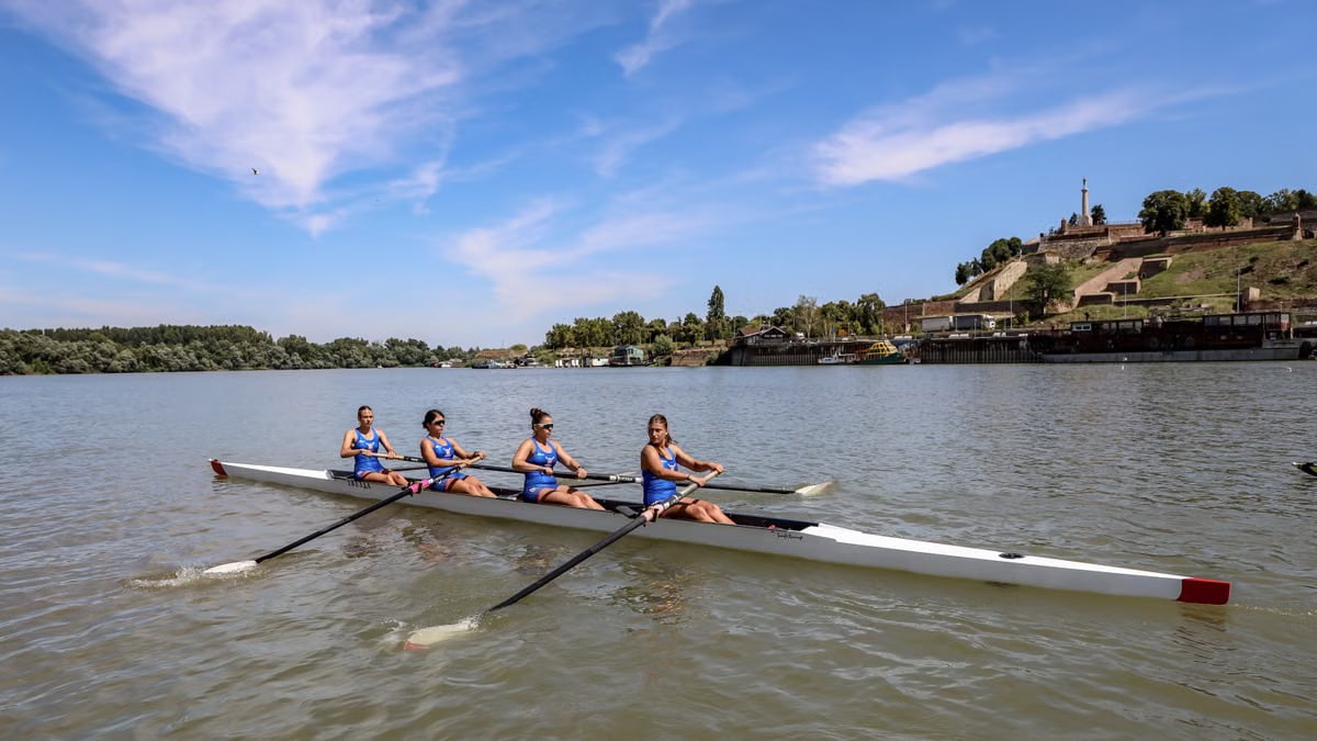 Four female rowers practicing on the Danube River in Belgrade, Serbia with Kalemegdan Fortress in the background.